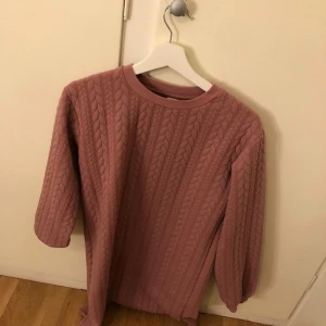 Rosa stickad tröja från Lindex - Mysig rosa stickad tröja från Lindex med kabelstickat mönster. Tröjan har trekvartsärmar och rund halsringning. Perfekt för kyliga dagar!