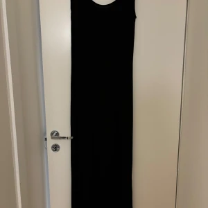 Svart långklänning - Elegant svart långklänning med ärmlös design. Perfekt för en stilren och tidlös look. Klänningen har en enkel och klassisk siluett som passar många tillfällen.