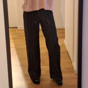 Svarta randiga kostymbyxor - Snygga svarta kostymbyxor med vita ränder. Byxorna har en loose passform vilket ger en stilren look. Perfekta för en chic och elegant stil. Är i storlek xxs