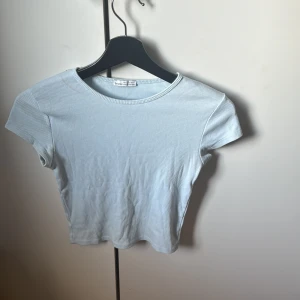 Ljusblå ribbad topp - Säljer en ljusblå ribbad topp med korta ärmar. Perfekt för en avslappnad stil. Toppen har en enkel och stilren design.
