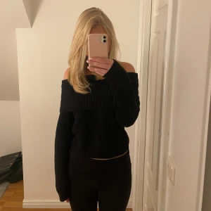 Svart stickad offshoulder tröja - Snygg svart stickad offshoulder tröja med ribbad design. Perfekt för en stilren look med långa ärmar och en croppad passform. Enkelt att matcha med olika outfits. Knappt använd.