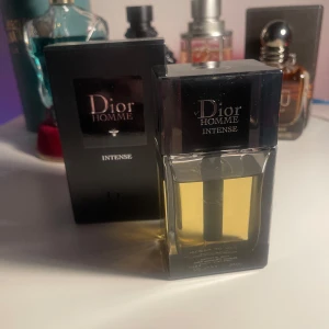 Dior Homme Intense Parfym - Säljer en elegant Dior Homme Intense parfym i en stilren glasflaska med svart lock. Doften är intensiv och maskulin, perfekt för den som vill sticka ut. Flaskan har en modern design med en gyllene vätska inuti. 46ml kvar.