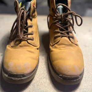 Bruna boots från Levi's - Säljer ett par bruna Levi’s kängor i storlek 38. Kängorna har en robust design med snörning och vadderat skaft för extra komfort. Sulan är mönstrad för bra grepp och märkt med Levi’s logga. Passar bra för höst- och vinterbruk.  Skick: Slitna med tydliga märken och skav på ovandelen samt mindre skador i materialet. Fortfarande funktionella.  Nypris:  1 200 SEK