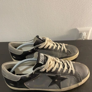 Golden Goose Superstar - Snygga sneakers från Golden Goose. Svarta och grå i läder som gör dem väldigt slittåliga. Skorna har en vintage-look från början.