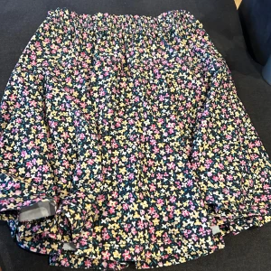 Blommig kortkjol med resårmidja - Säljer en superfin blommig kortkjol med resårmidja. köpt i istanbul, Kjolen har ett färgglatt mönster med små blommor i rosa, gult och vitt på en mörkblå bakgrund. Perfekt för sommaren eller en festlig tillställning! 🥳