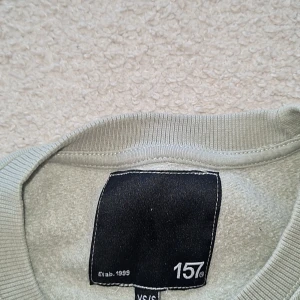 Grå sweatshirt från 157 - Säljer en enkel och stilren ljus grön sweatshirt från 157. Den är i storlek XS och passar perfekt för en avslappnad look. Tröjan är gjord av mjukt material och har långa ärmar samt en rund halsringning. Perfekt för höst och vinter!