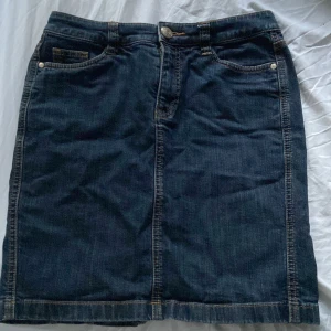 Jeanskjol från Esprit - Säljer en snygg jeanskjol från Esprit i storlek 36. Kjolen är i mörkblå denim med klassisk femficksdesign och knäppning fram. Baktill finns två fickor med knappar och en liten slits för extra rörelsefrihet. Perfekt för både vardag och fest!