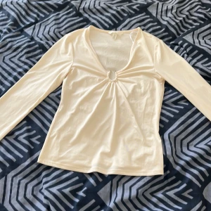 Beige långärmad topp med v-ringning - Säljer en snygg beige långärmad topp med v-ringning och en liten rynkdetalj framtill. Perfekt för både vardag och fest. Toppen är i storlek XS och är i ett mjukt och bekvämt material.