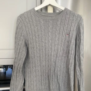 Grå stickad tröja från Gant - Säljer en snygg och bekväm grå kabelstickad tröja från Gant i storlek S. Tröjan är gjord av premium bomull. Perfekt för höst och vinter! Gott skick