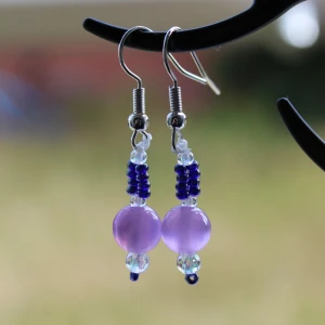 Lila och blå pärlörhängen - Säljer ett par superfina örhängen med lila och blå pärlor. De har en enkel krok för att hänga i örat och är perfekta för att ge en färgklick till din outfit. Passar både till vardag och fest!