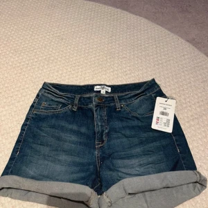 Mörkblå jeansshorts från H&M - Säljer ett par snygga mörkblå jeansshorts . De är i nyskick och har en klassisk femficksdesign med knapp och dragkedja framtill. Shortsen har en uppvikt kant nedtill som ger en cool look. Perfekta för sommaren! 🌞