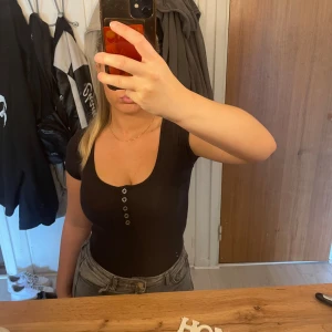 Svart ribbad bodysuit från Hollister - Säljer en svart ribbad bodysuit från Hollister i storlek XS. Jag har vanligtvis storlek S, men den är stretchig så passar både bra för folk som bär S och XS. Den har korta ärmar och en knappdetalj framtill som går att öppna om man vill det. Perfekt för både vardag och fest!