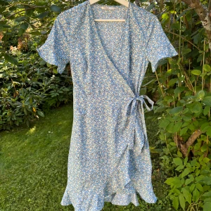 Only klänning  - Kort, ljusblå omlottklänning från Only med volangdetaljer och knytning i midjan. Normal passform med v-ringning. Används fåtal gånger  Nypris: 329 kr