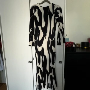 Svartvit långklänning med abstrakt mönster - Säljer en supercool svartvit långklänning med ett abstrakt mönster. Klänningen har långa ärmar och är gjord av ett ribbat material som ger en snygg struktur. Perfekt för fest eller andra speciella tillfällen. Den är i nyskick och har en normal passform. Passar perfekt för höst och vinter!