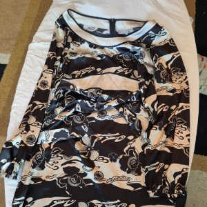 Svart och vit mönstrad klänning från Lindex - Säljer en snygg svart och vit mönstrad klänning från Lindex i storlek 40. Klänningen har långa ärmar och ett coolt blommigt mönster. Perfekt för både vardag och fest! Den är i bra skick och har en dragkedja i ryggen för enkel på- och avtagning.