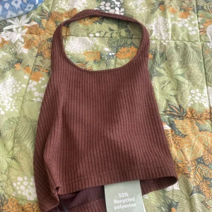 Brun ribbad linnetopp - Säljer en snygg brun ribbad linnetopp. Den är tillverkad av 52% återvunnen polyester och är perfekt för varma sommardagar. Toppen har en tight passform och är ärmlös, vilket gör den både bekväm och stilren.