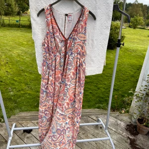 Klänning - Pasely mönstrad klänning med dekorativ urringning. Kortare fram. Helt ny