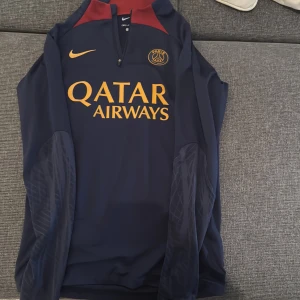 Paris Saint-Germain långärmad fotbollströja - Säljer en långärmad Paris Saint-Germain fotbollströja från Nike. Tröjan är mörkblå med röda detaljer och har en gul Nike-logga samt Qatar Airways som sponsor. Den är i slim fit och tillverkad med Dri-FIT material för att hålla dig torr och bekväm. Perfekt för både träning och vardagsbruk!