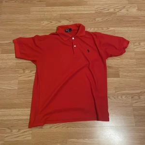 Röd pikétröja från Polo - Säljer en klassisk röd pikétröja från Polo i 100% bomull. Tröjan har en broderad logotyp på bröstet och korta ärmar. Perfekt för en stilren look.