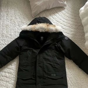 Svart parkajacka från Canada Goose - Säljer en svart parkajacka från Canada Goose med pälsfodrad huva. Jackan har en klassisk design med dragkedja och flera praktiska fickor. Perfekt för kalla dagar med sin varma och skyddande stil. 🖤