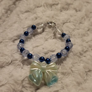 Armband med pärlor och rosett - Charmigt armband med blå och genomskinliga pärlor samt en stor dekorativ rosett i mitten. Perfekt för att ge en söt touch till din outfit.