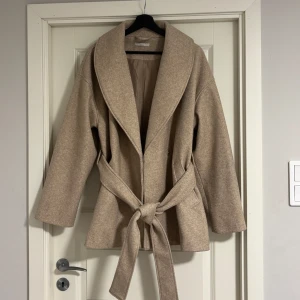Beige kappa med bälte - Lite nopprig på vissa ställen men det går att ta bort enkelt! Ny pris 700kr Snygg beige kappa med bälte och bred krage. Perfekt för höst och vår. Den har en stilren design med långa ärmar och en bekväm passform. Ett måste i garderoben för en chic look.