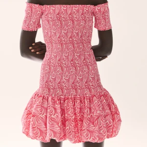 Rosa offshoulder klänning - Trendig rosa offshoulder klänning med ett livligt mönster. Klänningen har en volangdetalj vid fållen och korta ärmar. Perfekt för en somrig look!