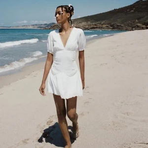 Vit kortklänning med v-ringning - Säljer en söt vit kortklänning med v-ringning och korta ärmar. Klänningen har en omlott-design och fina spetsdetaljer vid fållen. Perfekt för sommarens varma dagar! 