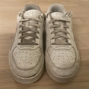 Vita sneakers från Puma - Säljer ett par vita sneakers från Puma med klassisk design och snörning. Skorna har en stilren look med perforerade detaljer på ovansidan och Puma-logga på hälen. Perfekta för en avslappnad stil. Skicka om du vill ha fler bilder. Först till kvarn