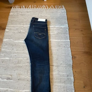 Mörkblå jeans från Replay - Snygga mörkblå jeans från Replay med klassisk femficksdesign och kontrastsömmar. Dessa jeans har en dragkedja och knapp framtill samt en stilren Replay-logga på bakfickan. Helt perfekta dem är i ny skick och har slim fit passform. Storlek 30:32