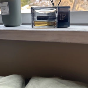 Dior Homme Intense Parfym - Säljer en elegant Dior Homme Intense parfym i en stilren glasflaska med svart kork. Doften är intensiv och maskulin, perfekt för den som vill sticka ut. Flaskan har en rektangulär form och innehåller en gyllene vätska.