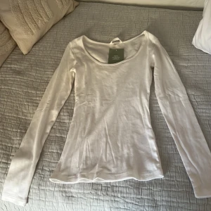 Vit långärmad topp från H&M - Säljer en stilren vit långärmad topp från H&M. Perfekt för lager-på-lager eller att bära som den är. Toppen har en rund halsringning och är tillverkad i ett mjukt material.