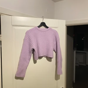 Lila ribbad croppad tröja - Säljer en snygg lila croppad tröja med ribbad struktur. Tröjan har långa ärmar och en hög halsringning, perfekt för en trendig look. Passar utmärkt till både jeans och kjol. Perfekt för höst och vår!