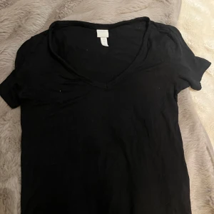 Svart v-ringad t-shirt - Säljer en klassisk svart t-shirt med v-ringning. Perfekt basplagg för alla tillfällen. Kortärmad och i mjukt material för bekväm passform.