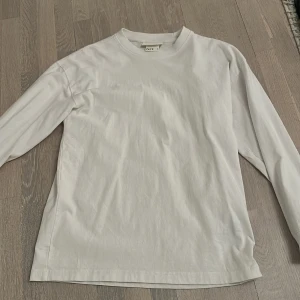 Vit långärmad tröja från ARKET - Säljer en stilren vit långärmad tröja från ARKET. Perfekt för en minimalistisk look. Tröjan är tillverkad i mjuk bomull och har en klassisk passform. Ett måste i garderoben för alla som älskar enkelhet och komfort.