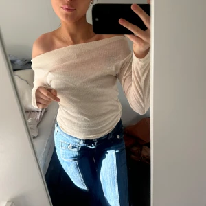 Beige offshoulder topp - Snygg beige offshoulder topp med ribbad design. Perfekt för en stilren och trendig look. Toppen har långa ärmar och en tight passform som framhäver figuren.