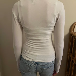 Vit långärmad topp från Nelly - Säljer en stilren vit långärmad topp från Nelly i storlek XS. Toppen har en tight passform och är perfekt för lager-på-lager eller att bära som den är.  Design som passar till många olika outfits. Den har en grå fläk på mitten av framsidan som knappt syns men kan vara bra att vetta. 💕