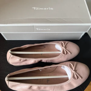 Rosa ballerinaskor från Tamaris - Säljer ett par eleganta rosa ballerinaskor från Tamaris. Skorna har en söt rosett på ovansidan och är tillverkade i ett mjukt material som ger en bekväm passform!💕