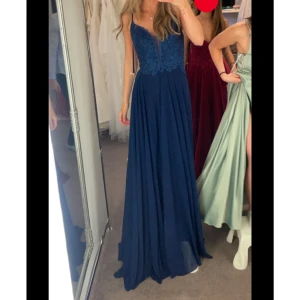 Marinblå Balklänning med snörning i ryggen - Marinblå balklänning med spetsdetaljer på överdelen och öppen rygg med snörning. Storlek 38 men passar mig som vanligtvis har 34-36 då den går att spänna åt i snörningen. Jag är 172 cm. Klänningen har även litet släp. Det är insydda bh kupor!🌸💕💕