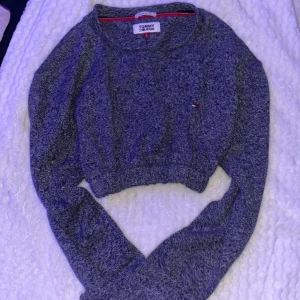 Grå croppad tröja från Tommy Jeans - Säljer en snygg grå croppad tröja från Tommy Jeans som jag köpt på Urban Outfiters för ca 400kr. Tröjan har långa ärmar och en avslappnad passform med elastisk nederkant. Storlek L men passar bra på mig som är XS. 