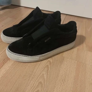 Svarta sneakers från Axel Arigato - Snygga svarta sneakers från Axel Arigato i mocka med en stilren design. Skorna har en vit sula som ger en fin kontrast och en diskret logga på sidan. Perfekta för en trendig look.