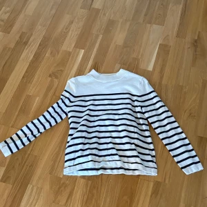 Randig tröja från Hampton Republic - Säljer en stilren randig tröja från Hampton Republic i vitt och svart. Tröjan har långa ärmar och knappar på axeln för en extra detalj. Perfekt för en avslappnad och klassisk look.