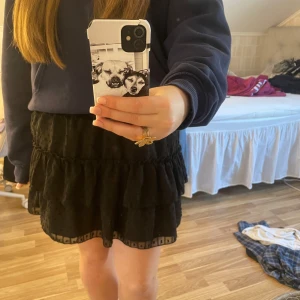 Svart volangkjol - Säljer en söt svart kortkjol med volanger och prickigt mönster. Kjolen har en elastisk midja för bekväm passform och är perfekt för att ge en lekfull touch till din outfit. Passar bra till både vardag och speciella tillfällen.