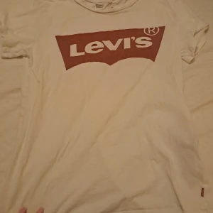 Vit t-shirt från Levi's - Säljer en klassisk vit t-shirt från Levi's med det ikoniska röda logotyptrycket på framsidan. T-shirten är kortärmad och tillverkad i mjuk bomull. Perfekt för en avslappnad stil.