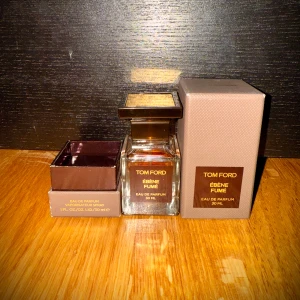 Ébène Fumé Eau de Parfum från Tom Ford - Säljer en elegant flaska av Tom Ford Ébène Fumé Eau de Parfum, 30 ml. Flaskan har en stilren design med en fyrkantig form och ett brunt lock. Förpackningen är i en matchande brun nyans med guldtext. 80% kvar.