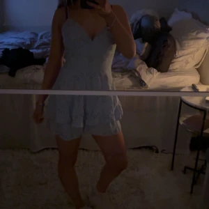 Ljusblå klänning med spetsdetaljer - Säljer en söt ljusblå klänning med spetsdetaljer och smala axelband. Klänningen har en v-ringad design och kort längd, perfekt för sommarens varma dagar. Den har en fin passform som framhäver figuren. Det är shorts i