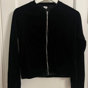 Svart sammet kofta - Snygg svart kofta i mjuk sammet med dragkedja framtill. Perfekt för en stilren look. Koftan har långa ärmar och en klassisk passform. Storlek 158/164 men passar xxs-s