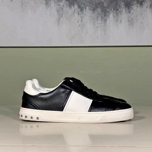 Valentino Flycrews skor - Snygga svartvita sneakers med en stilren design och dekorativa nitar på sulan. Skorna har en vit sula och svart snörning, vilket ger en klassisk look. Perfekta för en trendig stil. Storlek 43 
