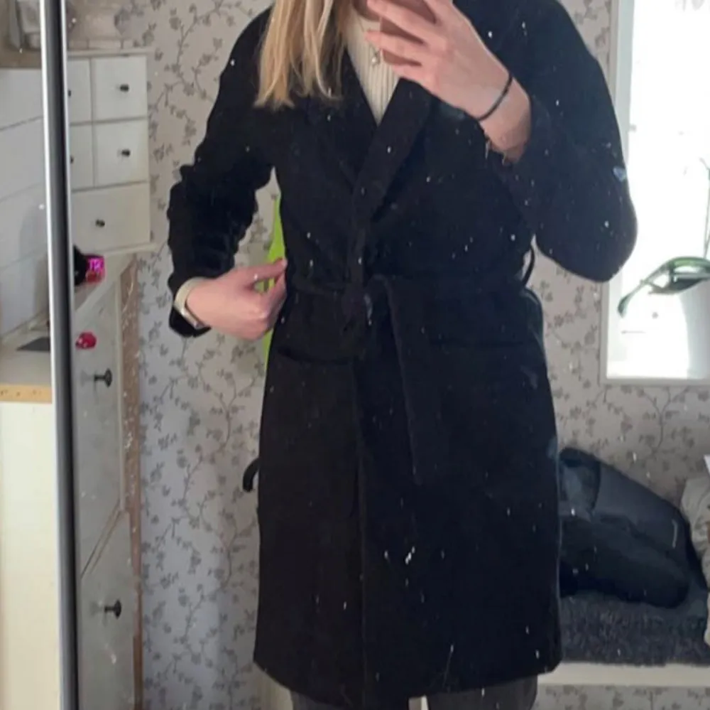 Snygg svart lång kappa med bälte som ger en elegant look, köpt från Gina. Perfekt för kyligare dagar med sin stilrena design och långa ärmar. Trendig och snygg🩷🩷Jag är 175. Takit.