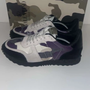 Valentino Rockrunner i camouflage - Snygga Valentino Rockrunner sneakers med ett coolt camouflage-mönster i lila, beige och svart. Skorna har snörning och är tillverkade i en kombination av skinn och syntetmaterial. Perfekta för att ge din outfit en unik touch.